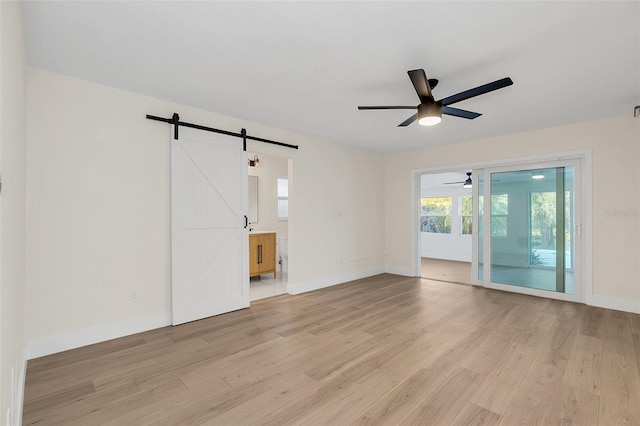 spare room featuring ceiling fan, a barn door, and light hardwood / wood-style flooring