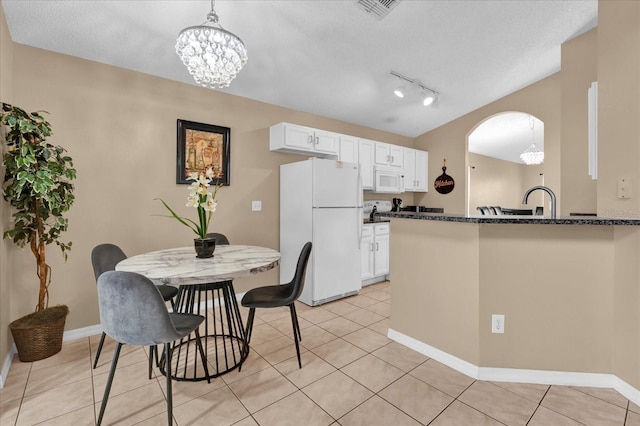 kitchen with kitchen peninsula, white appliances, a notable chandelier, dark stone countertops, and white cabinetry