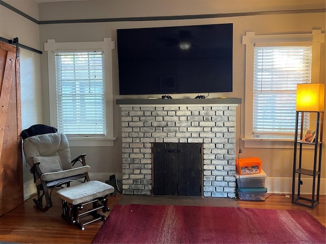 living room with a barn door, wood-type flooring, and a brick fireplace