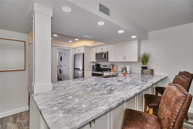 kitchen with a kitchen breakfast bar, kitchen peninsula, stacked washer and dryer, appliances with stainless steel finishes, and white cabinetry