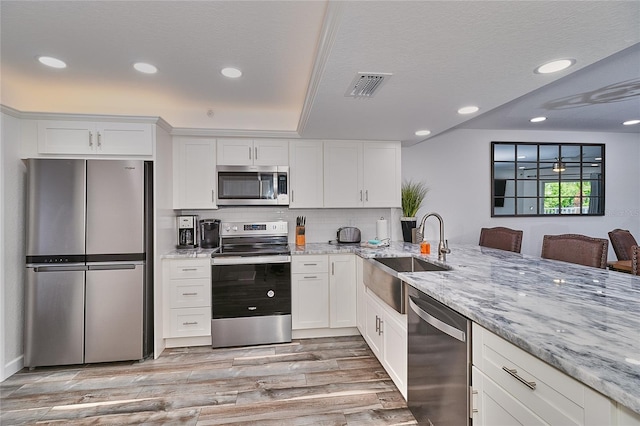 kitchen featuring white cabinetry, sink, stainless steel appliances, light hardwood / wood-style floors, and a breakfast bar area