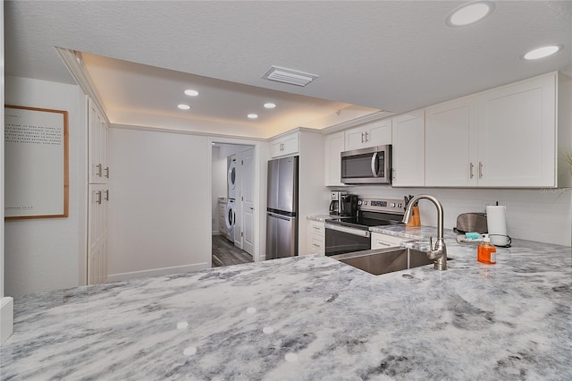 kitchen featuring white cabinets, sink, stacked washer and dryer, tasteful backsplash, and stainless steel appliances