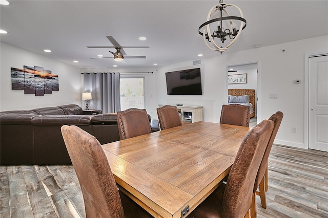 dining space with ceiling fan with notable chandelier and hardwood / wood-style flooring