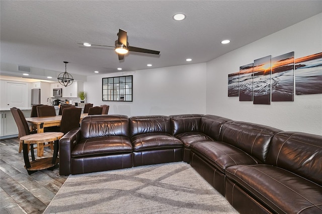 living room featuring ceiling fan with notable chandelier, a textured ceiling, and hardwood / wood-style flooring