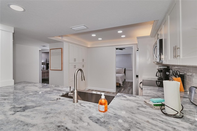 18400 Gulf Blvd Unit 1206, Indian Shores, FL 33785 - kitchen featuring stainless steel microwave, a raised ceiling, light stone counters, white cabinetry, and recessed lighting