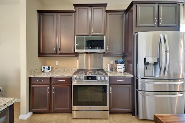 kitchen featuring light stone countertops, appliances with stainless steel finishes, light tile patterned floors, and dark brown cabinets