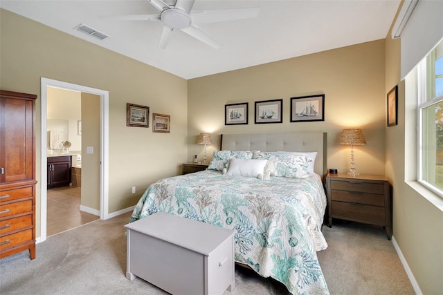 carpeted bedroom with ceiling fan, ensuite bathroom, and multiple windows