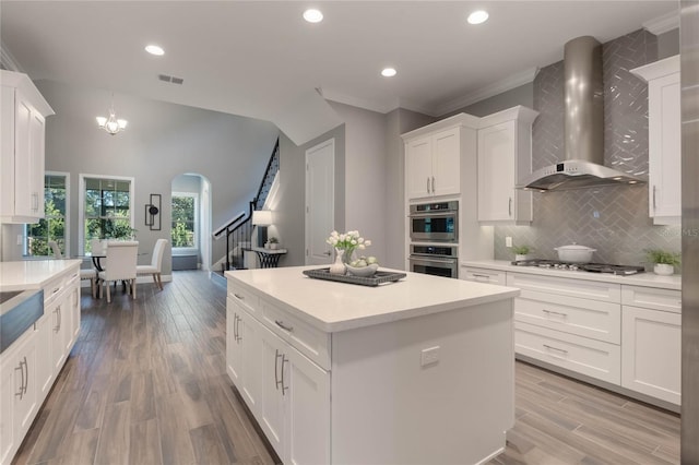 kitchen with a center island, hardwood / wood-style flooring, wall chimney exhaust hood, appliances with stainless steel finishes, and white cabinetry