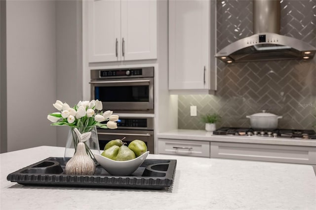 kitchen with light stone countertops, tasteful backsplash, stainless steel appliances, wall chimney range hood, and white cabinetry