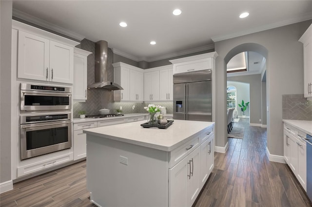 kitchen with white cabinets, wall chimney exhaust hood, dark wood-type flooring, and appliances with stainless steel finishes