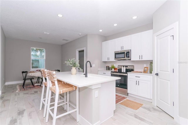 kitchen with appliances with stainless steel finishes, white cabinetry, a kitchen island with sink, and sink