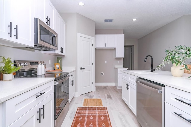 kitchen with appliances with stainless steel finishes, light wood-type flooring, a textured ceiling, sink, and white cabinets