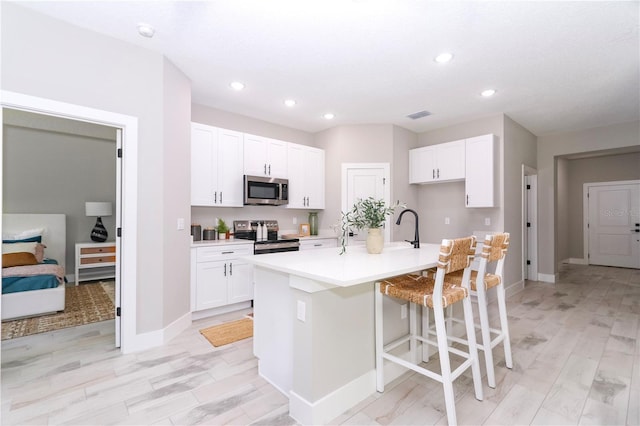 kitchen featuring a kitchen bar, appliances with stainless steel finishes, light hardwood / wood-style flooring, white cabinets, and an island with sink