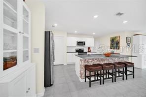 kitchen featuring white cabinets, a kitchen bar, stainless steel appliances, and a center island with sink