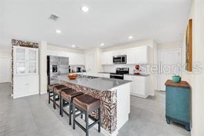 kitchen featuring a kitchen bar, white cabinetry, an island with sink, and stainless steel appliances