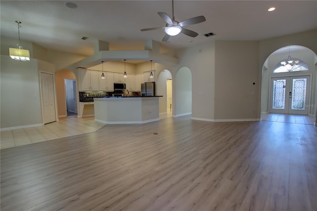 unfurnished living room with ceiling fan with notable chandelier, light wood-type flooring, and french doors