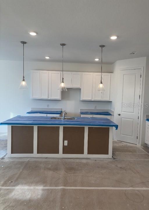 kitchen featuring white cabinets, a center island with sink, hanging light fixtures, and sink