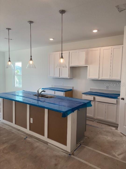 kitchen featuring a center island, white cabinetry, hanging light fixtures, and sink