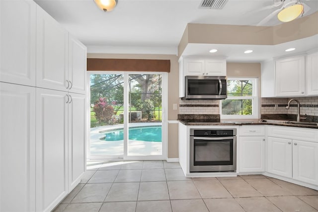 kitchen featuring decorative backsplash, appliances with stainless steel finishes, sink, white cabinetry, and light tile patterned flooring