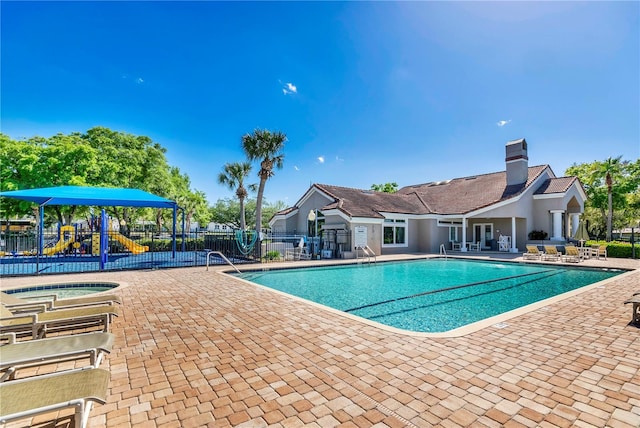 view of swimming pool featuring a community hot tub, a playground, and a patio area