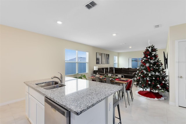 kitchen featuring light stone countertops, white cabinets, sink, dishwasher, and an island with sink