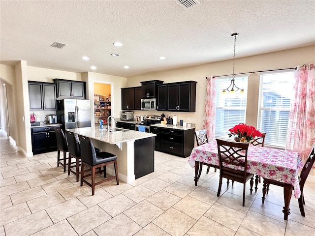 kitchen with stainless steel appliances, an island with sink, pendant lighting, a textured ceiling, and a breakfast bar area