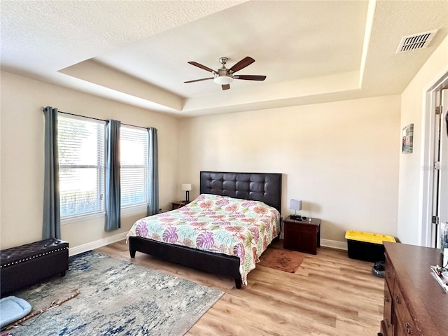 bedroom featuring ceiling fan, a tray ceiling, and light hardwood / wood-style flooring