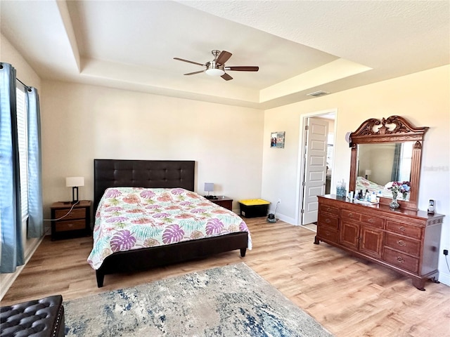 bedroom with ceiling fan, light wood-type flooring, and a tray ceiling