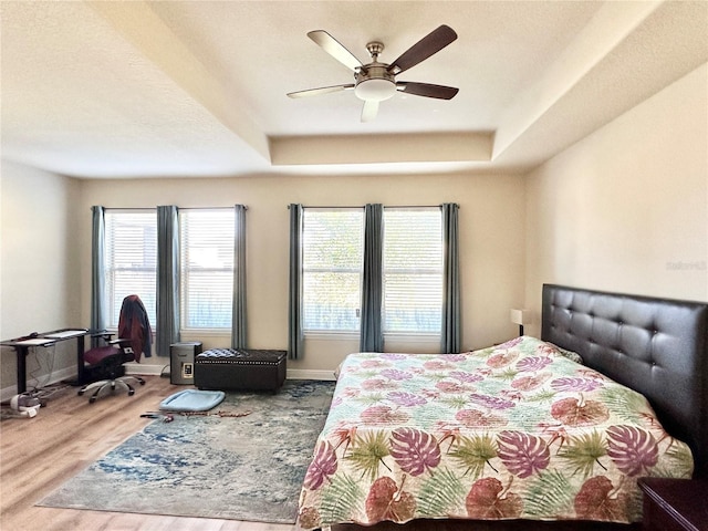 bedroom with hardwood / wood-style floors, a textured ceiling, a raised ceiling, and ceiling fan