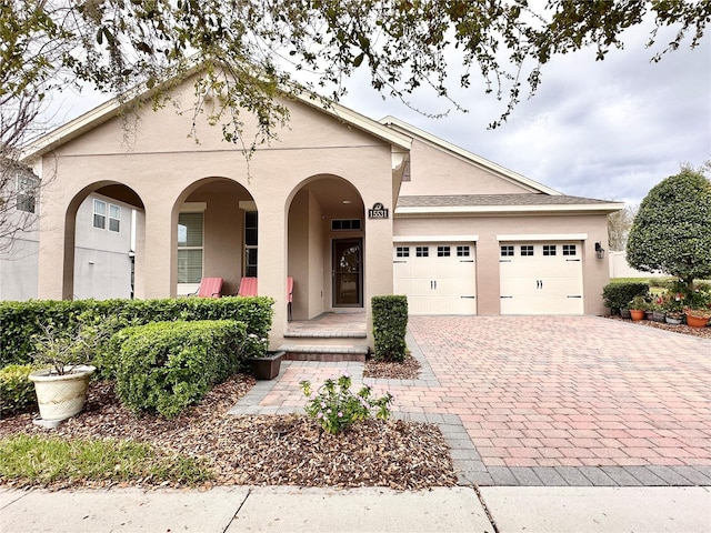 view of front of house with stucco siding, decorative driveway, a porch, and an attached garage