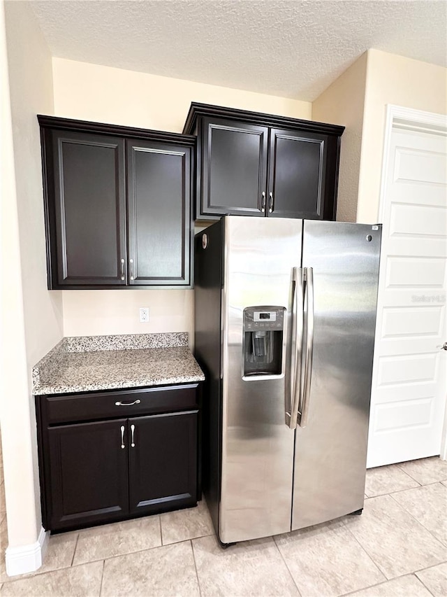 kitchen with dark cabinetry, stainless steel fridge with ice dispenser, light stone countertops, and a textured ceiling