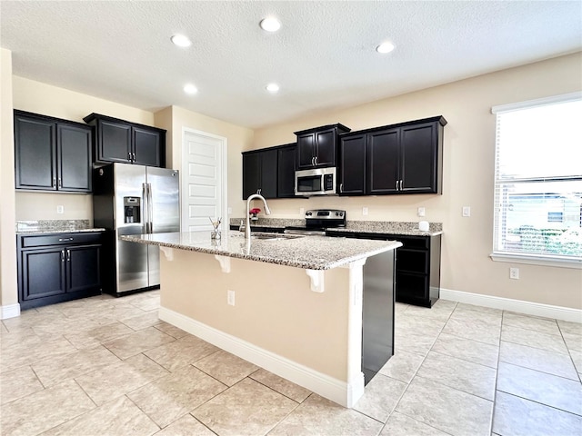 kitchen featuring a breakfast bar, a sink, light stone counters, dark cabinetry, and stainless steel appliances