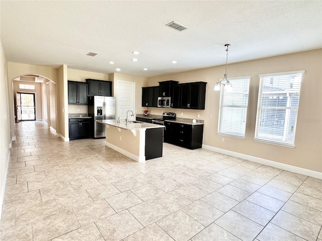 kitchen featuring visible vents, a sink, dark cabinetry, stainless steel appliances, and arched walkways