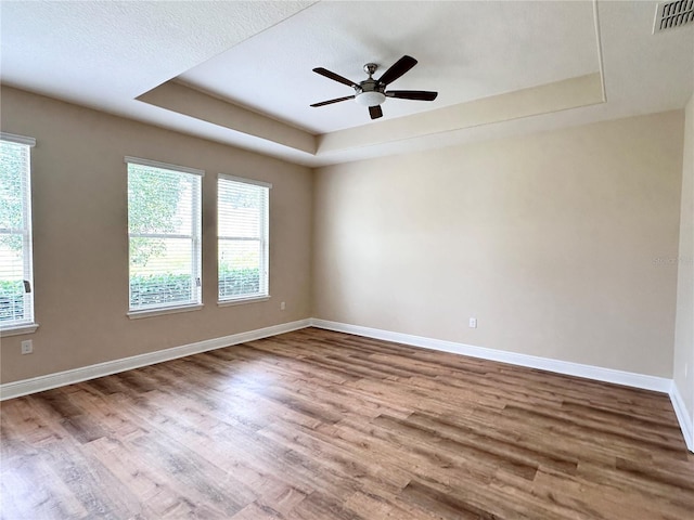 spare room featuring a tray ceiling, wood finished floors, baseboards, and visible vents