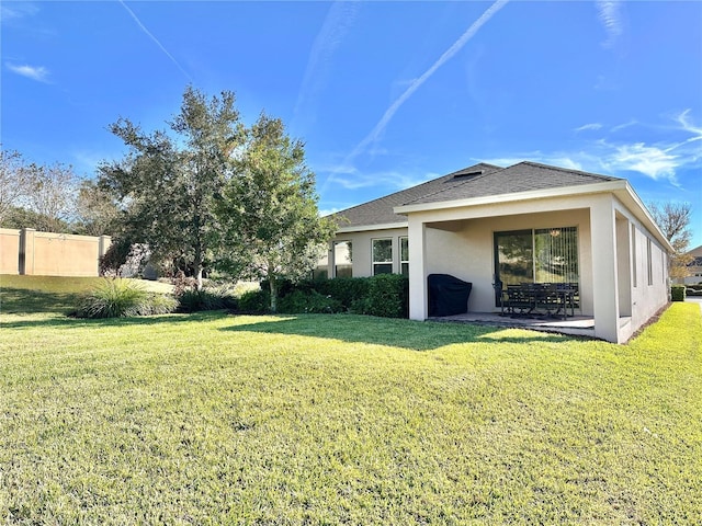 exterior space featuring stucco siding, a lawn, fence, roof with shingles, and a patio area