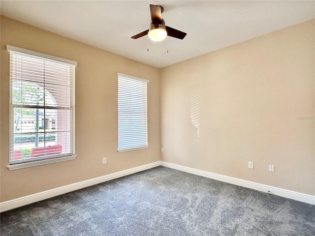 unfurnished room with a ceiling fan, baseboards, and dark colored carpet