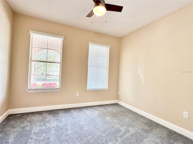 spare room with dark colored carpet, baseboards, and ceiling fan