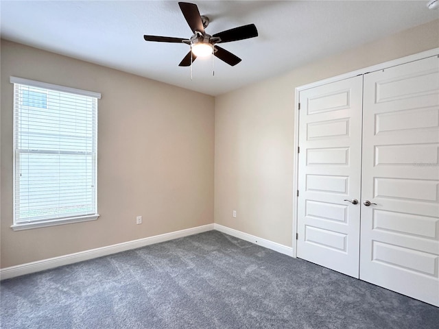 unfurnished bedroom with baseboards, dark colored carpet, a closet, and ceiling fan