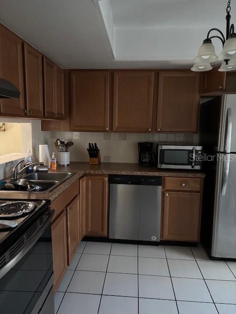 kitchen featuring exhaust hood, sink, light tile patterned floors, appliances with stainless steel finishes, and a notable chandelier