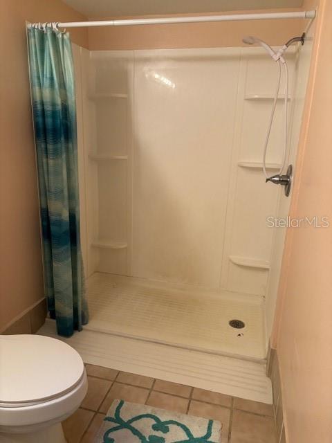 bathroom featuring curtained shower, tile patterned flooring, and toilet