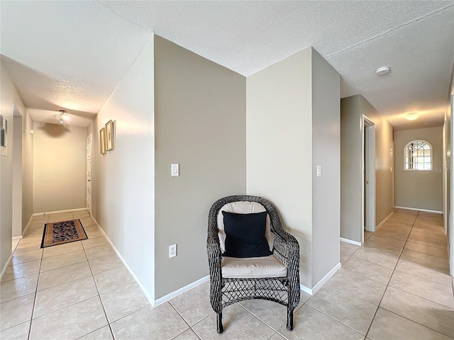 hallway featuring light tile patterned floors, a textured ceiling, and baseboards