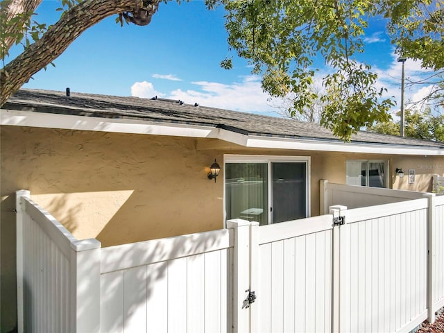 view of side of home featuring roof with shingles, fence, and stucco siding