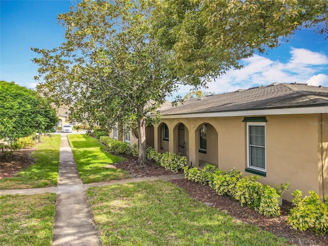 view of front facade featuring a shingled roof, a front lawn, and stucco siding