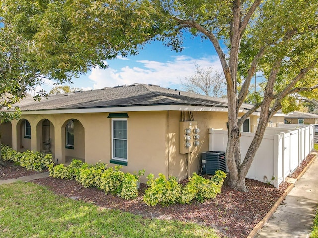 view of home's exterior featuring central AC unit, roof with shingles, fence, and stucco siding