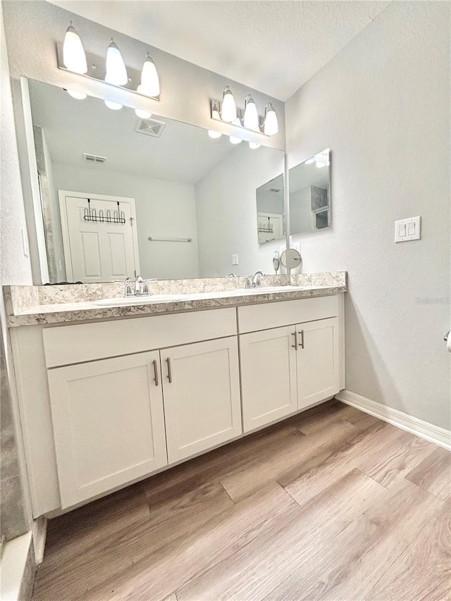 bathroom with double vanity, a sink, baseboards, and wood finished floors