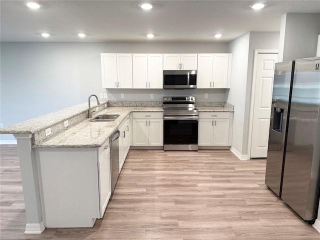 kitchen with stainless steel appliances, light wood finished floors, a peninsula, and a sink