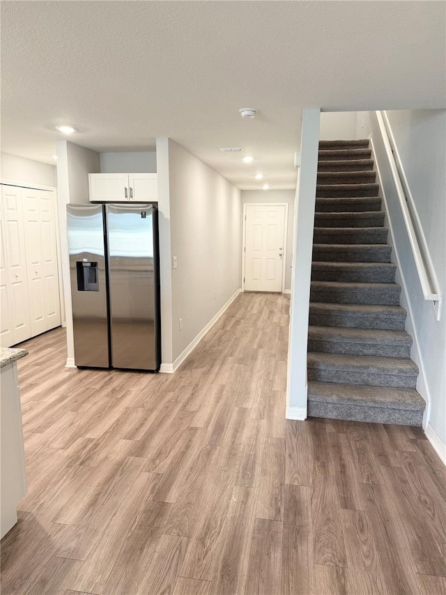 interior space featuring baseboards, a textured ceiling, light wood-style floors, white cabinetry, and stainless steel refrigerator with ice dispenser