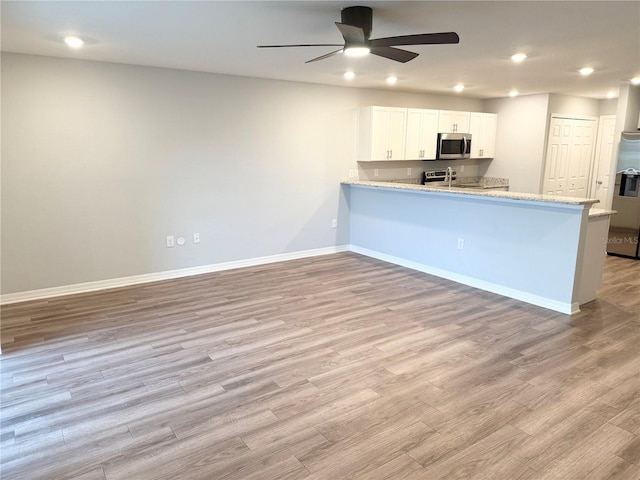 kitchen with baseboards, appliances with stainless steel finishes, a peninsula, light wood-style floors, and white cabinetry