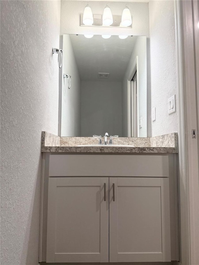 bathroom featuring visible vents, a textured wall, and vanity