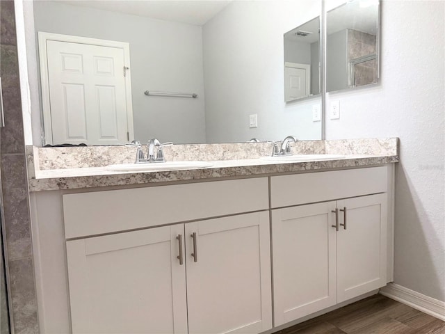 full bathroom with double vanity, a sink, baseboards, and wood finished floors